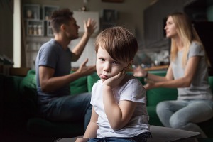 An upset child with parents fighting in the background who may need a Child Custody Lawyer in East Peoria IL